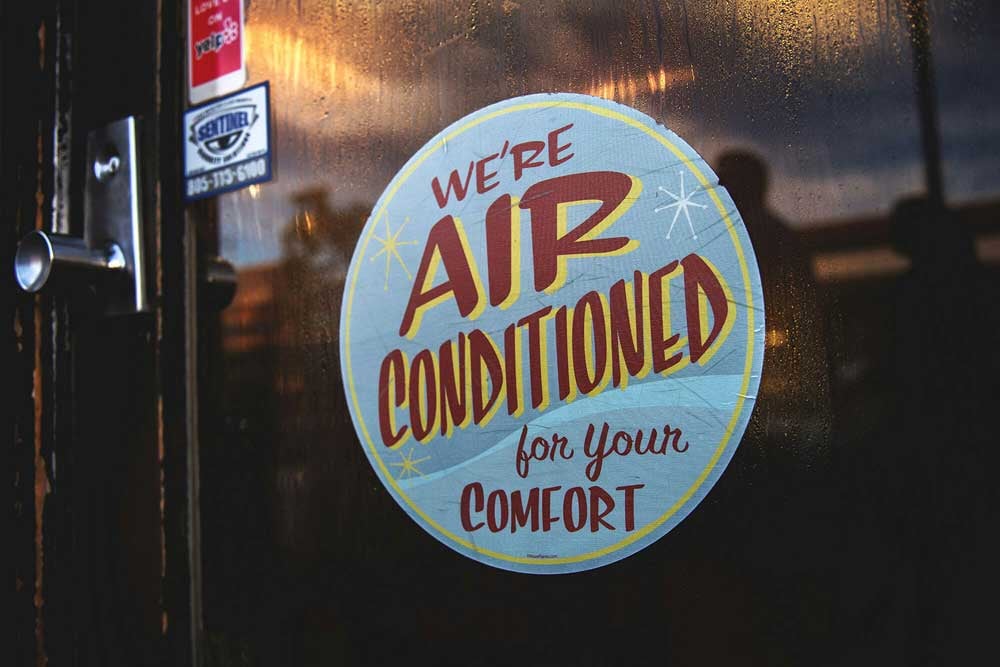 A round sign on a door that reads, WE RE AIR CONDITIONED for your comfort.