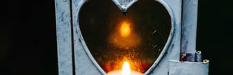 A lantern with a heart-shaped opening. Inside the lantern, there is a candle that emits a warm, glowing light. 