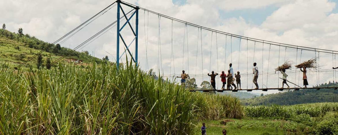People in rewanda walking over bridge carrying things