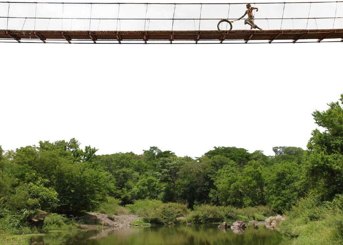 child rolls a wheel across bridge in rewanda