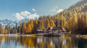 A serene image of two houses on a lake in the alps.  It appears to be late fall or early winter.