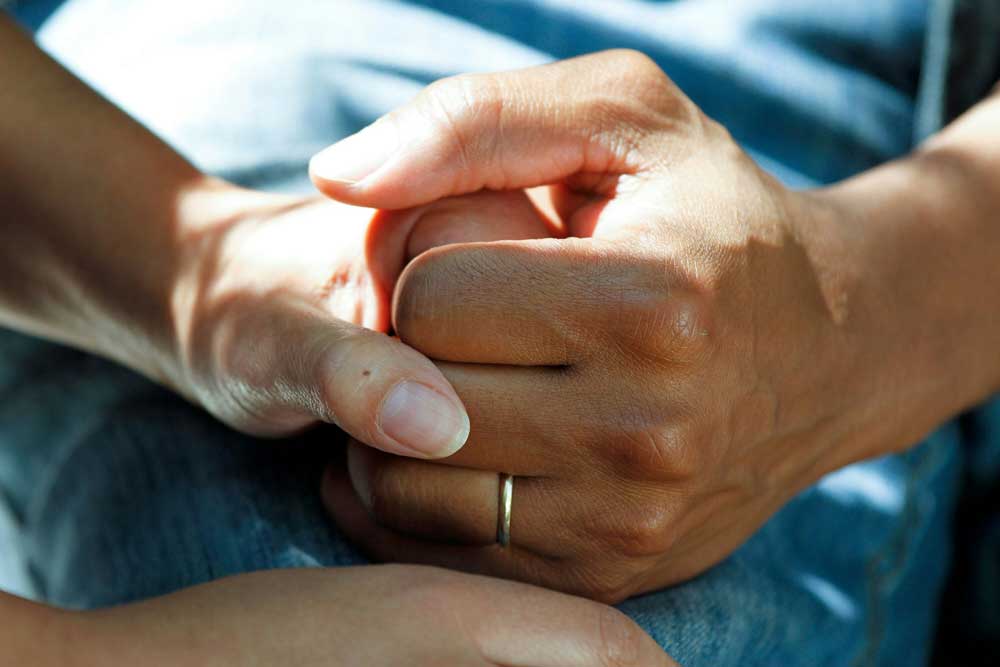 Two hands holding each other. One hand has a ring on it.